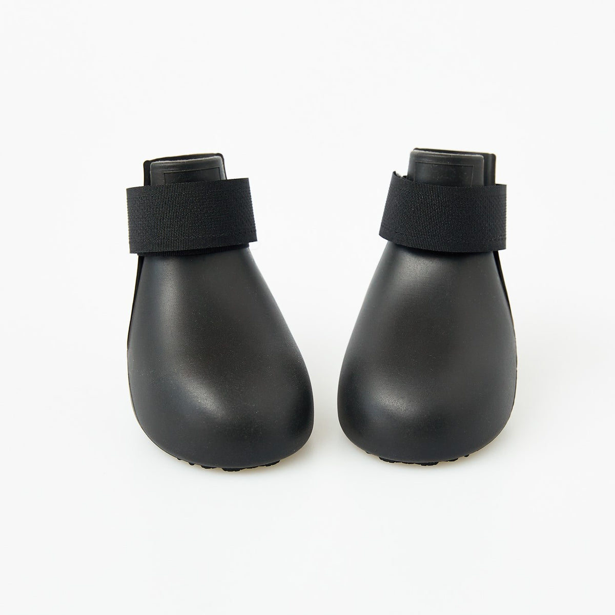 Small dog wearing bright silicone rain boots on a wet pavement